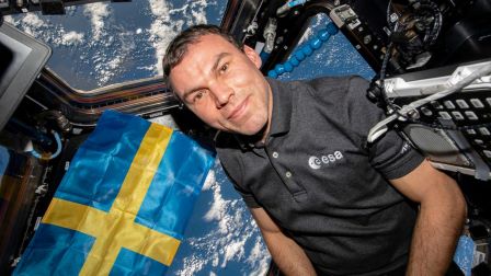 Astronaut håller upp svensk flagga i rymden.