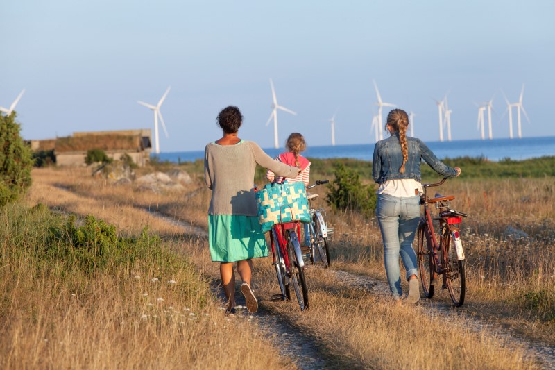 Tre personer leder sina cyklar. Vindkraftverk i bakgrunden.